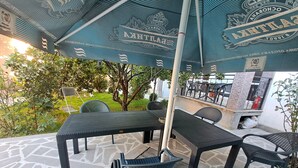 An outdoor patio area with a table and chairs under a blue umbrella, surrounded by greenery and a stone floor. - Guest House Akhaltsikhe (Akhaltsikhe)