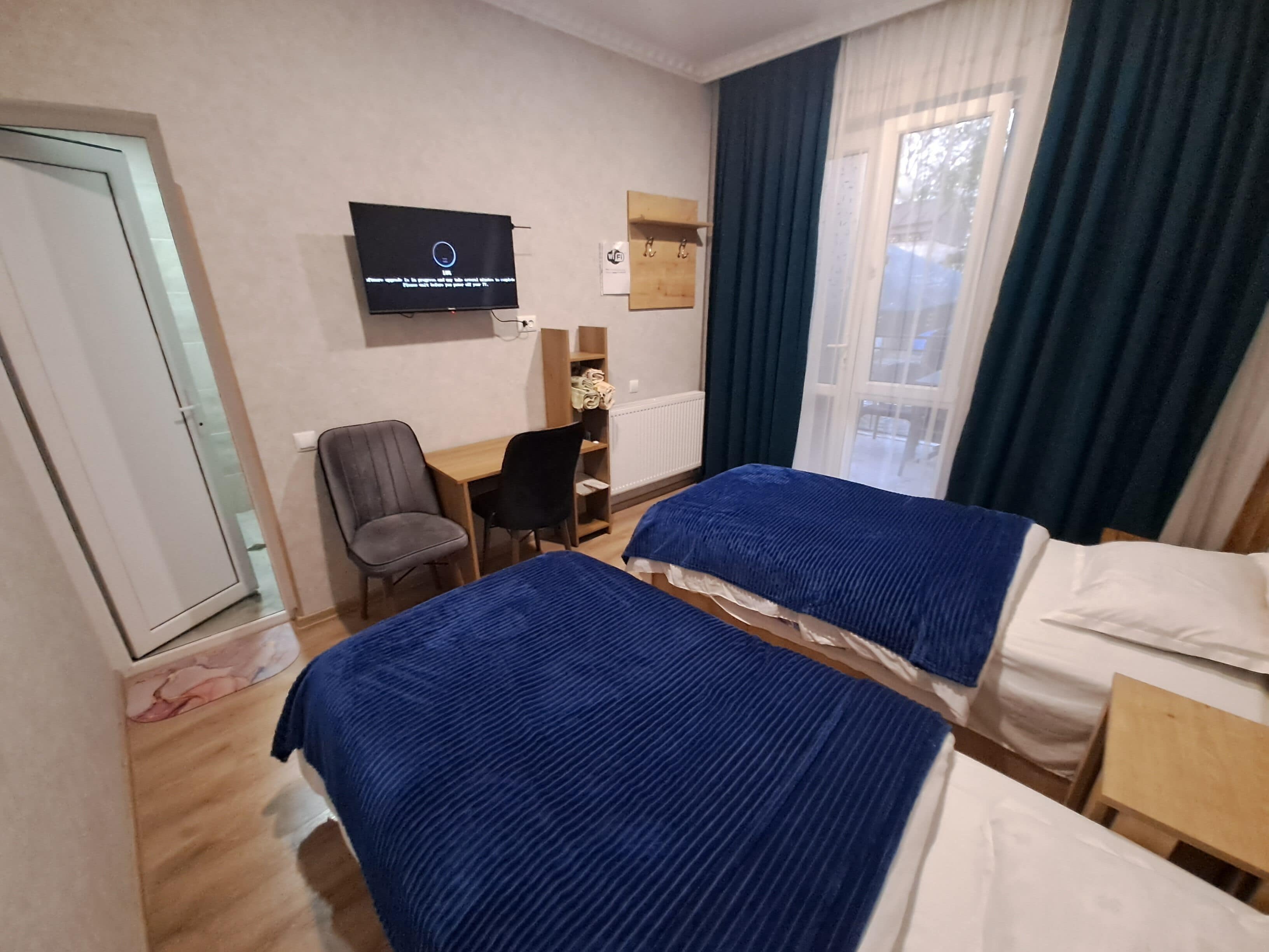 Ein Hotelzimmer mit zwei Betten, einem Schreibtisch, einem Stuhl, einem Fernseher und einem Vorhangfenster.