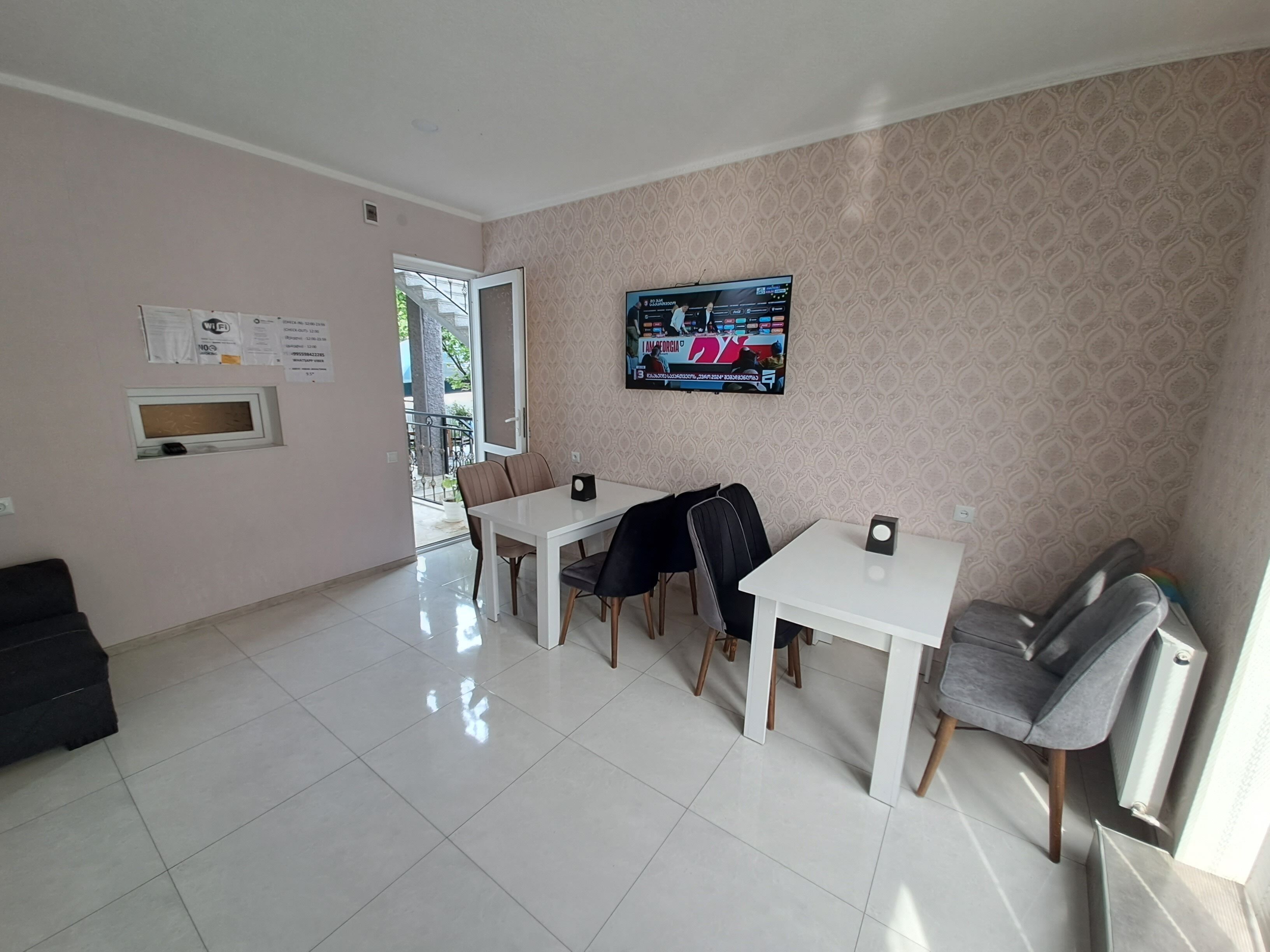 Una habitación con una mesa de comedor, sillas, un televisor montado en la pared y un ventanal con vistas al exterior.