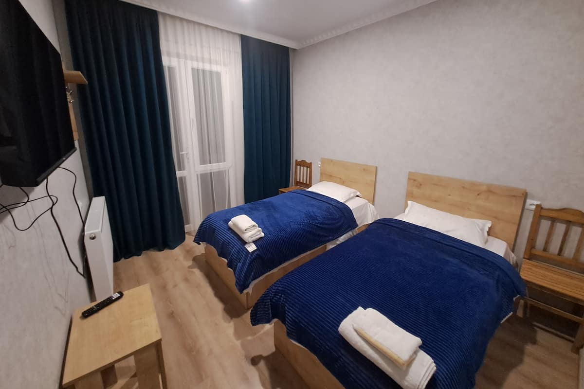 A hotel room with two beds, a TV, and a window with curtains.