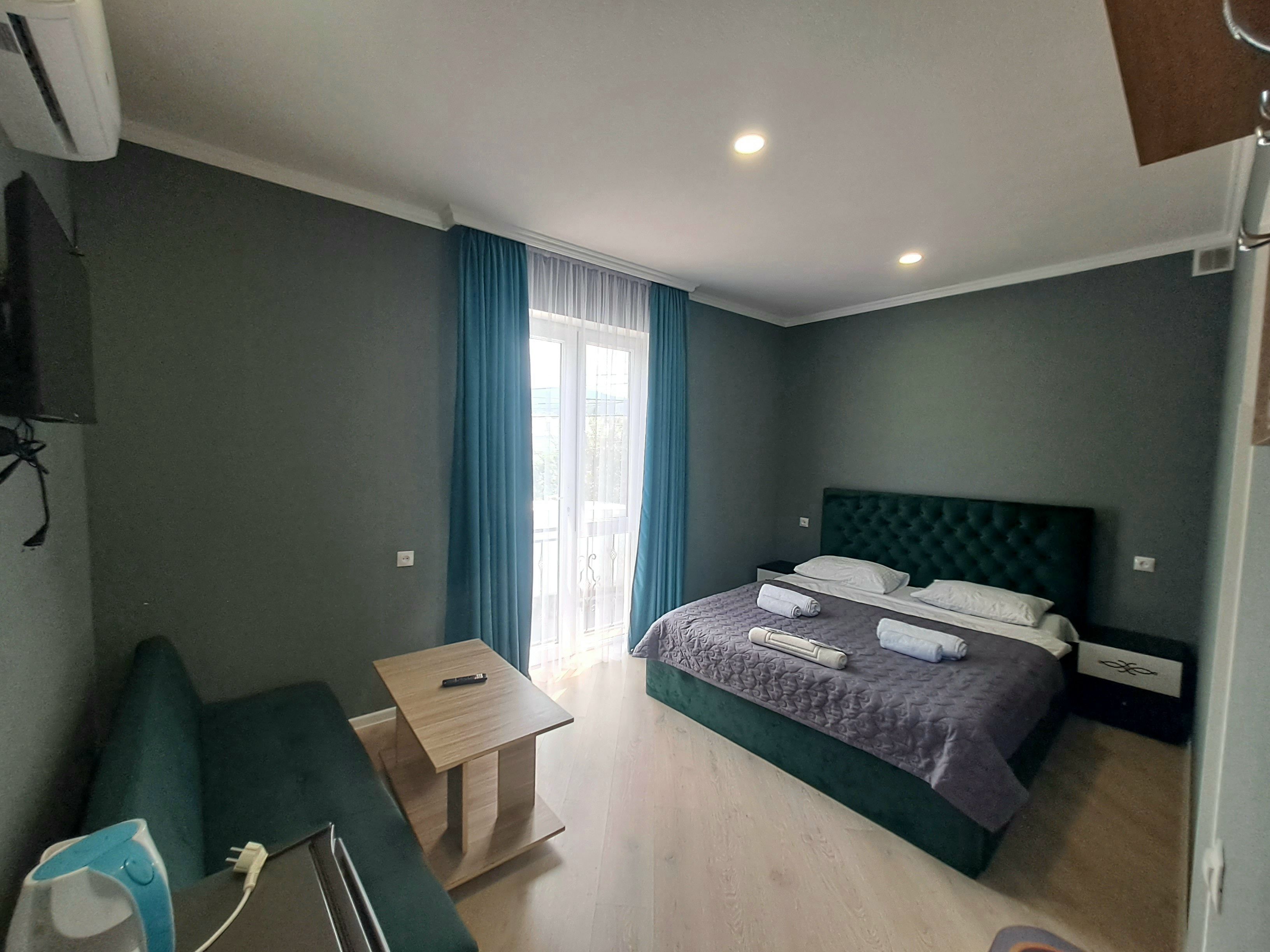 Una habitación de hotel con cama, una mesita, un sofá y un ventanal con cortinas.