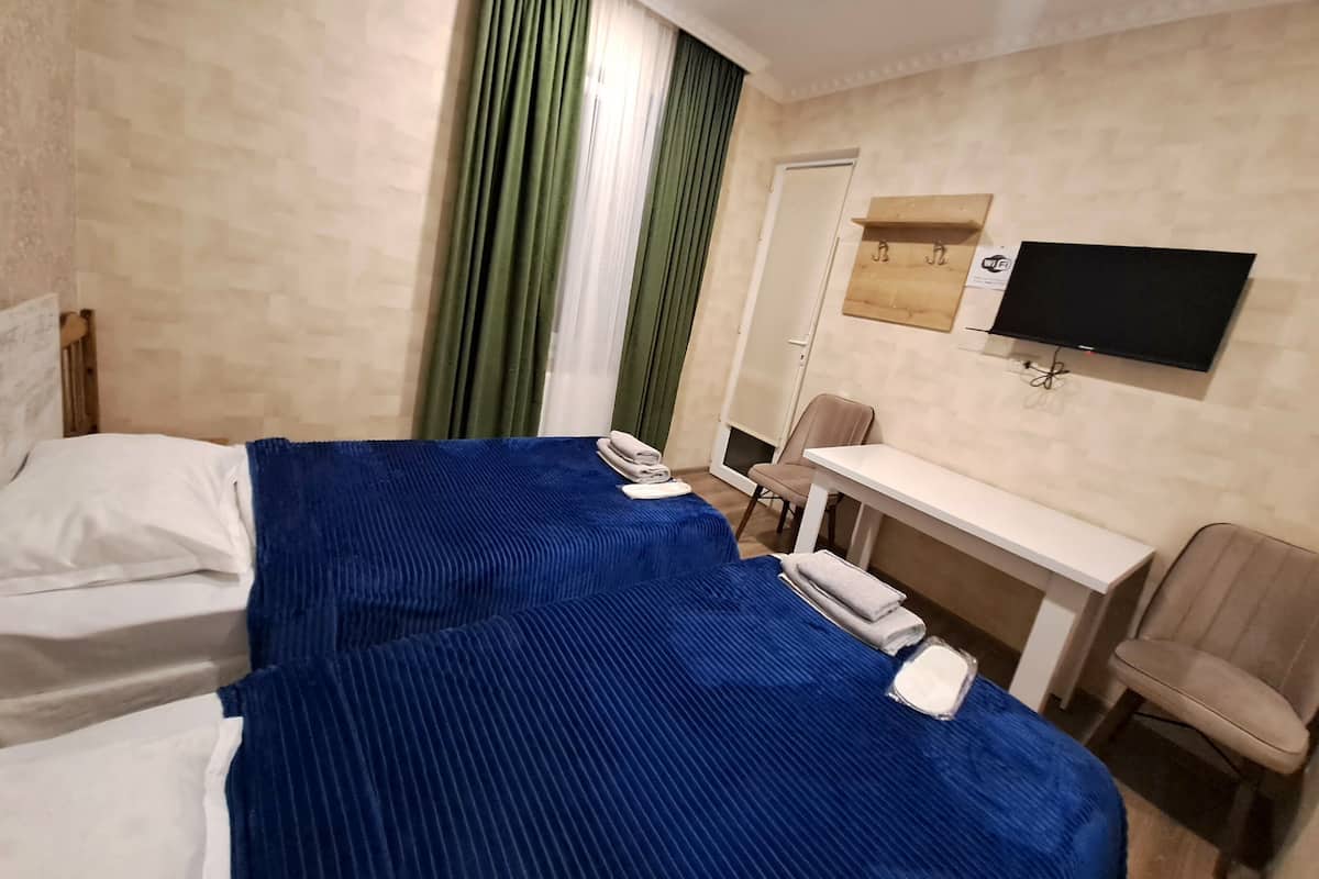 A hotel room with two beds, a desk, a chair, a TV, and a window with curtains.