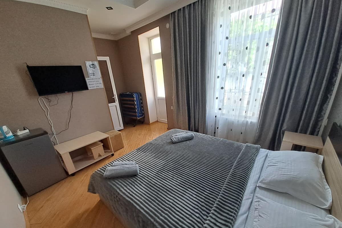 A hotel room with a bed, a desk, a TV mounted on the wall, and a window with curtains.