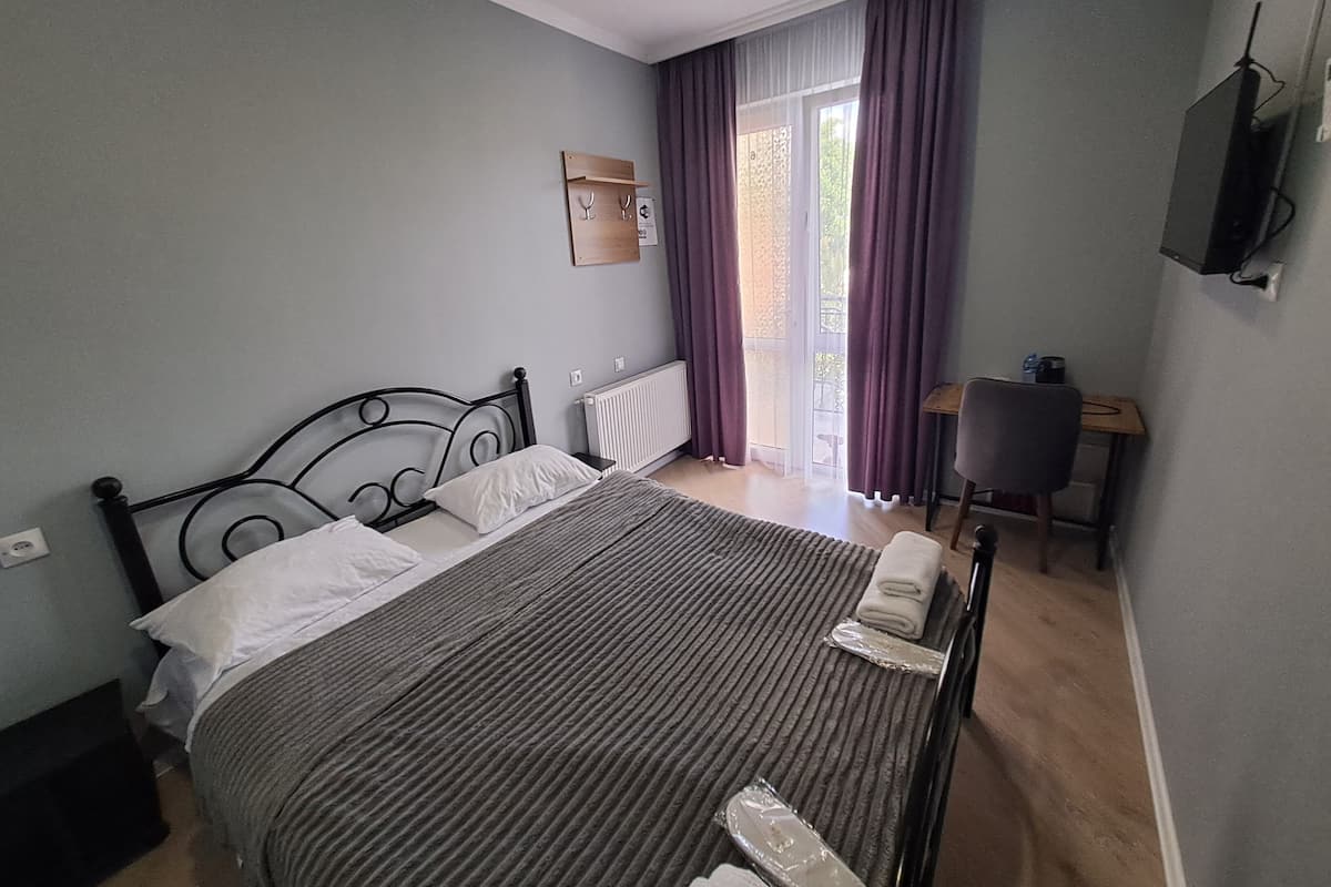 A bedroom with a bed, a desk, a chair, a radiator, and a window with curtains.
