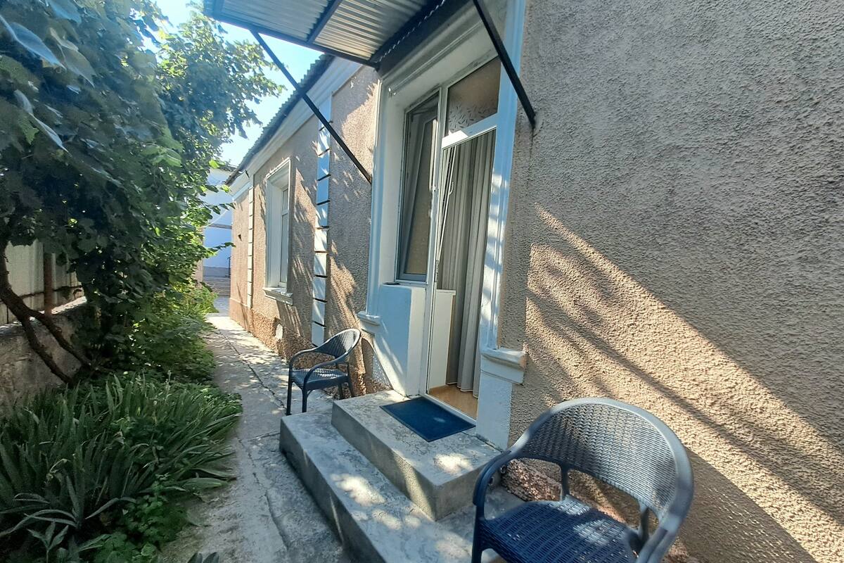 A narrow outdoor corridor with steps leading to a door, a chair, and a small table.