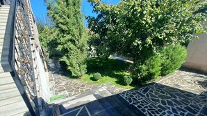 A courtyard with a stone-tiled floor, surrounded by trees and a small lawn. - Guest House Akhaltsikhe (Akhaltsikhe)