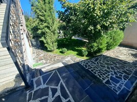 A courtyard with a stone-tiled floor, surrounded by trees and a small lawn.