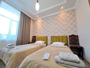 A hotel room with two beds, a large window with curtains, a patterned wallpaper, and a ceiling light. - Guest House Akhaltsikhe (Akhaltsikhe)