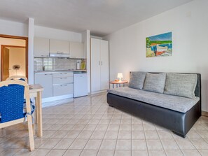 A compact living space with a kitchenette, a sofa, a dining table with chairs, and a small side table with a lamp.