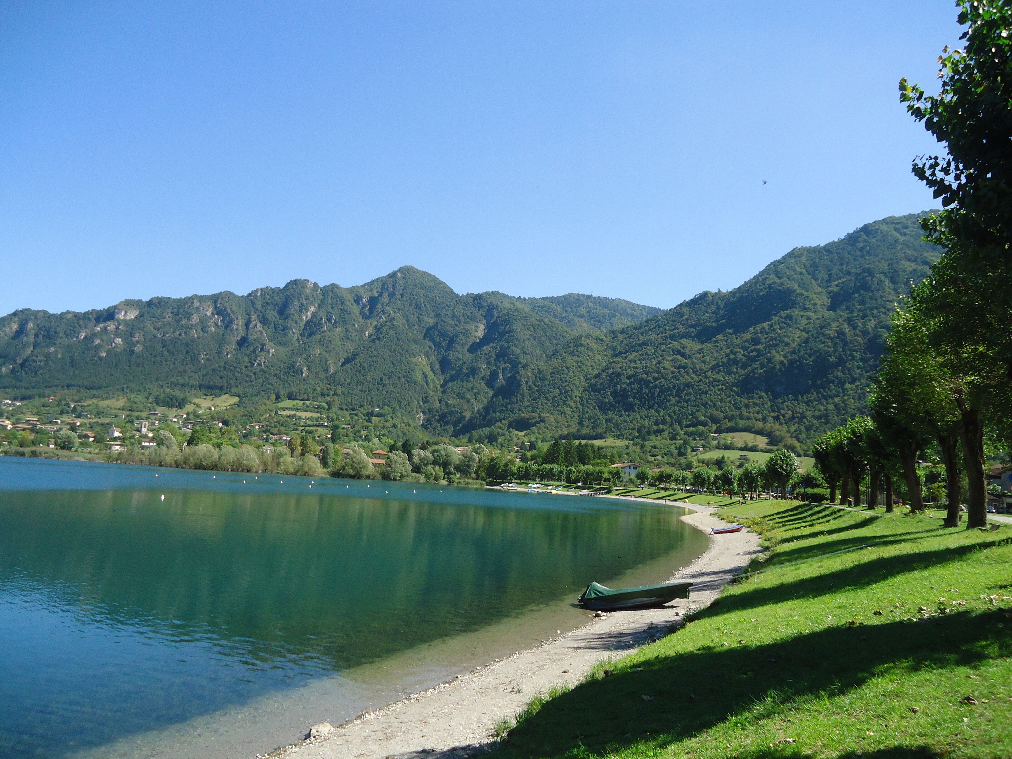 Une vue sur le lac, avec un bateau amarré sur la rive, entouré d’une végétation luxuriante et de montagnes en arrière-plan.