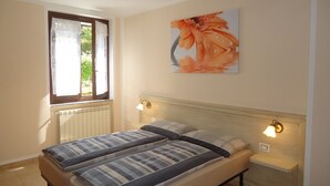 A bedroom with two beds, a window with curtains, a radiator, and a wall-mounted light fixture. - Ground floor apartment up to 6 pers., 3 bedrooms, terrace and garden, 300m to the lake (Crone)