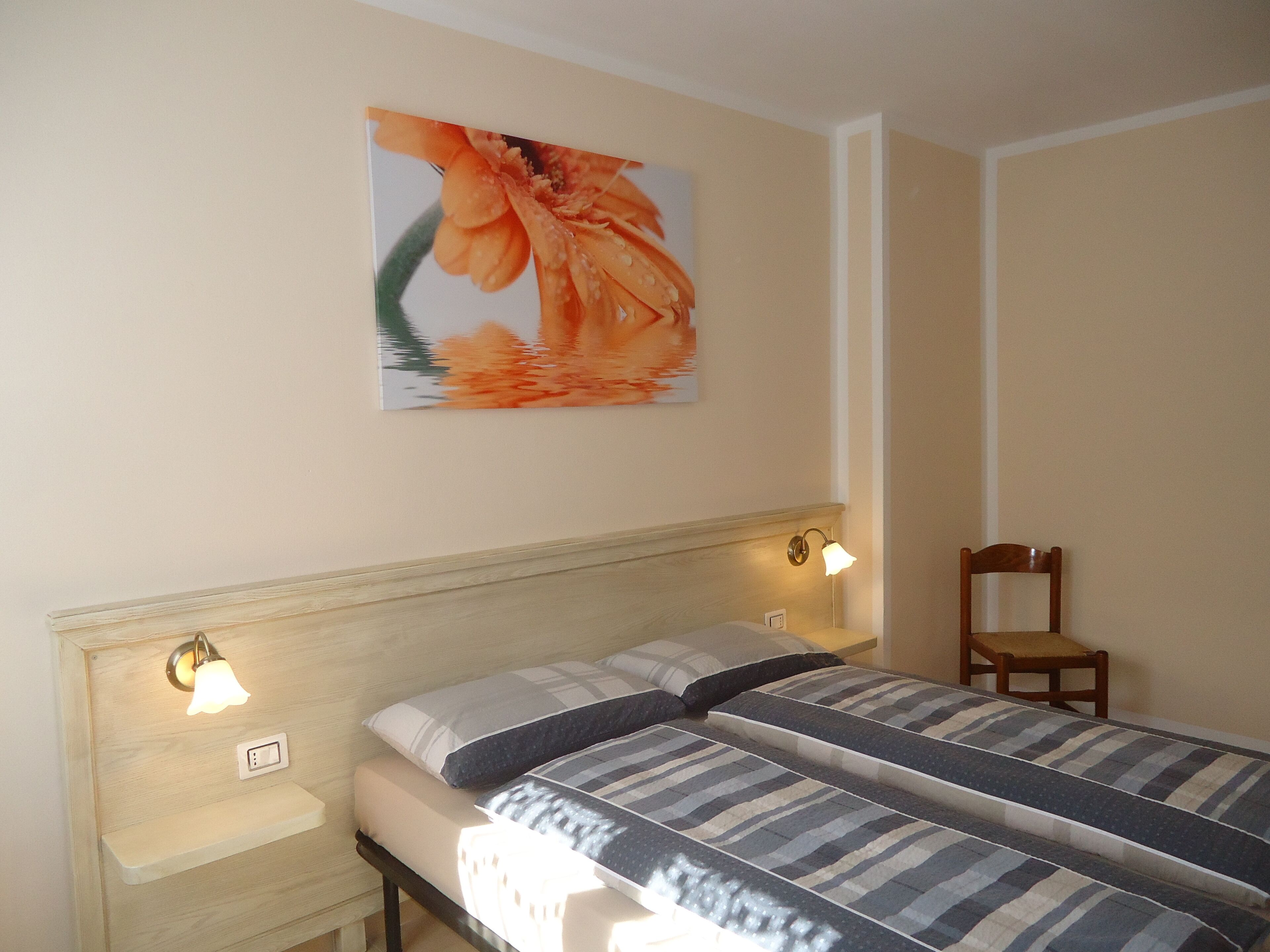 A bedroom with two beds, a nightstand, a chair, and a wall-mounted lamp.