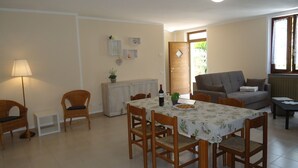 A dining area with a table set for four, a sofa, and a lamp. - Ground floor apartment up to 6 pers., 3 bedrooms, terrace and garden, 300m to the lake (Crone)