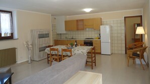 A compact kitchen with wooden cabinets, a dining area with a table and chairs, and a refrigerator. - Ground floor apartment up to 6 pers., 3 bedrooms, terrace and garden, 300m to the lake (Crone)