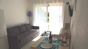 Una sala de estar con un sofá, una mesa de comedor preparada con platos, vasos y una botella, y un televisor montado en la pared.
