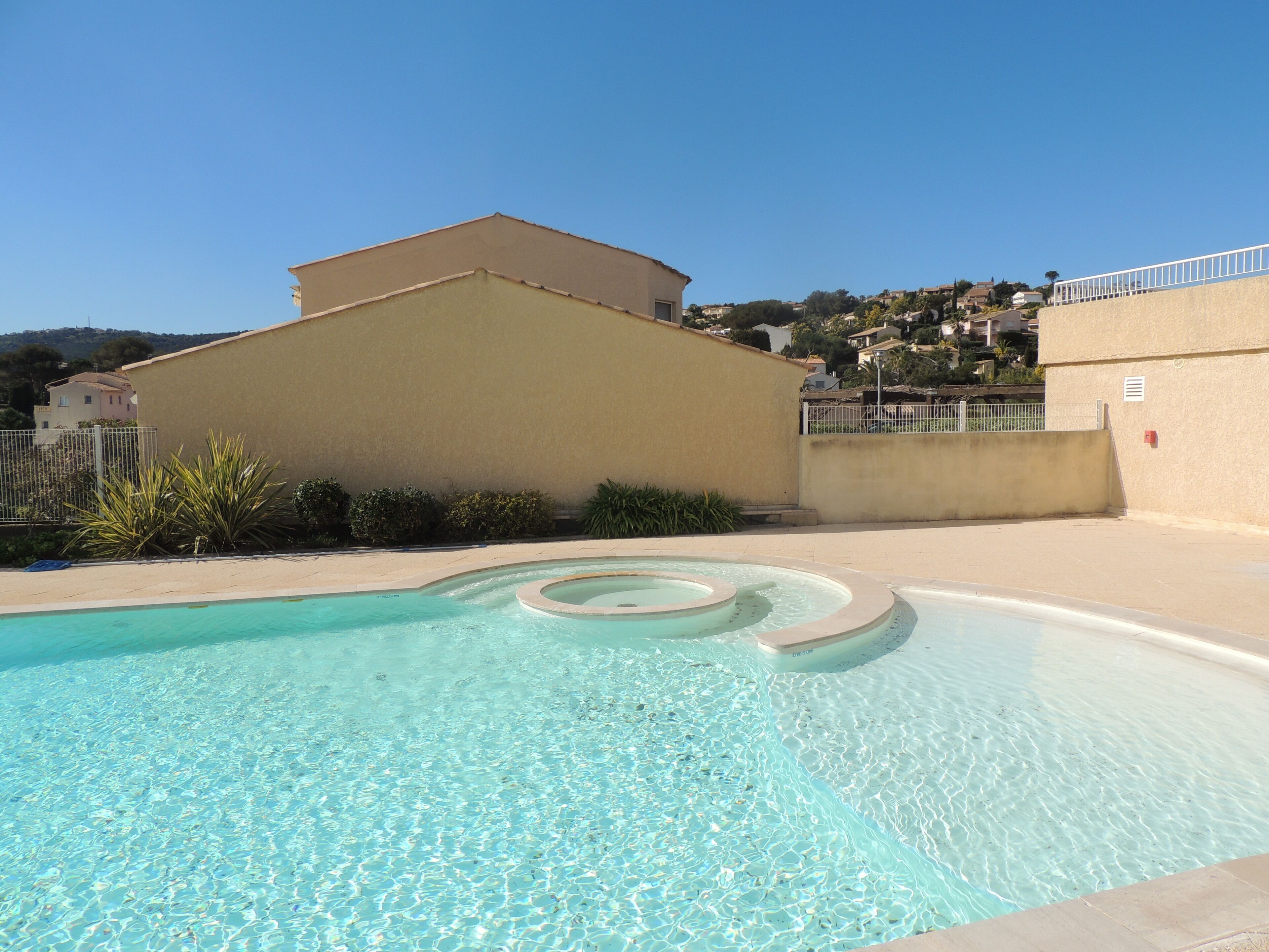 A clear swimming pool with a simple design, surrounded by a low wall and a fence.