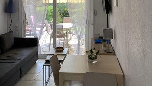Una sala de estar con un sofá, una mesa de comedor con sillas, un televisor montado en la pared y un equipo de aire acondicionado.