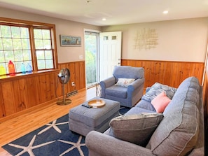 A living room with a wooden paneled wall, a grey sofa, a blue armchair, and a star-patterned rug.