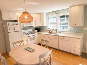 A kitchen with white cabinets, a wooden dining table, and a hanging light fixture.