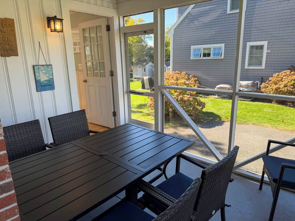 Un patio cubierto con una mesa y sillas, una puerta que da al exterior y vistas a una casa y jardín.