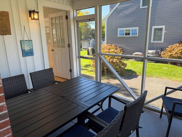 A covered patio with a table and chairs, a door leading outside, and a view of a house and lawn.