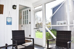 A room with two wicker chairs, a white door, and a view of a house through a glass door.