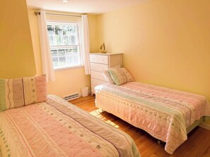 A bedroom with two single beds, a dresser, and a window with curtains.