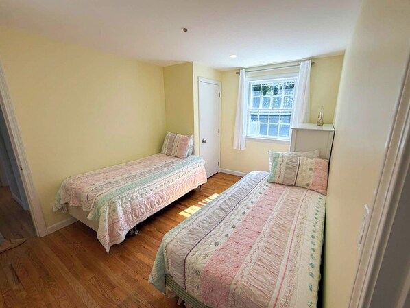 Una habitació amb dos llits individuals, una finestra amb cortines i una porta.