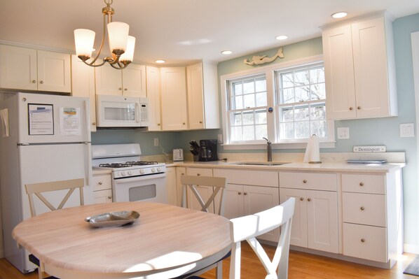 A kitchen with white cabinets, a stove, a microwave, and a dining table with chairs.