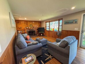 A living room with a sofa set, a fireplace, a television, and a large window with a view.
