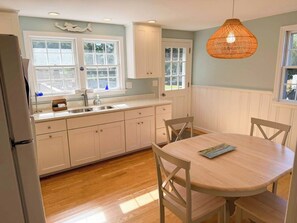 A kitchen with white cabinets, a wooden dining table, and a hanging light fixture.