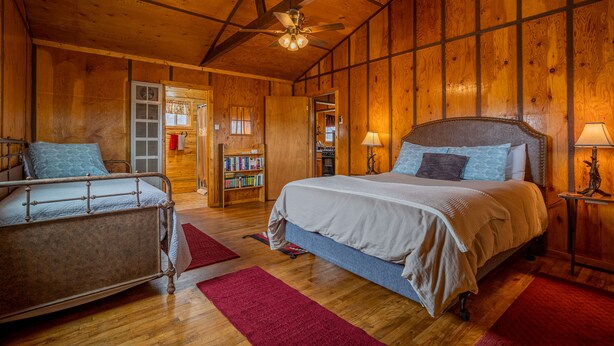 Een slaapkamer in een houten chalet, met een bed, een stoel, een boekenkast en een plafondventilator.