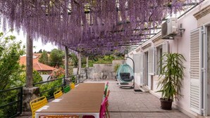Une terrasse extérieure couverte, avec une table et des chaises en bois, un fauteuil suspendu et une plante en pot.