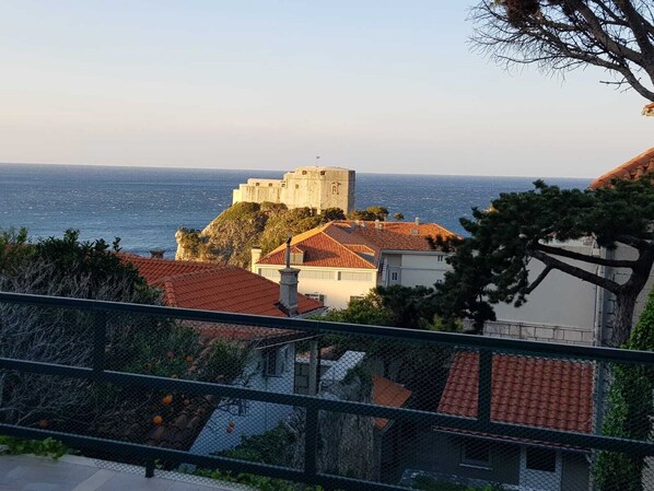 A coastal view with a historic stone building, red-roofed houses, and a clear sea.