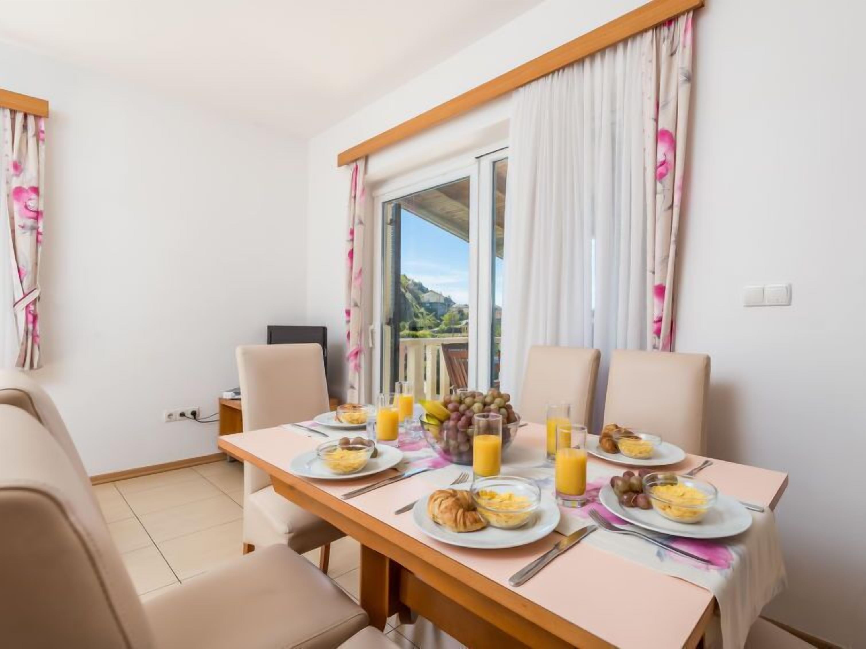 Une table de petit-déjeuner dressée avec des assiettes, des croissants et des fruits, et une vue magnifique par la fenêtre.