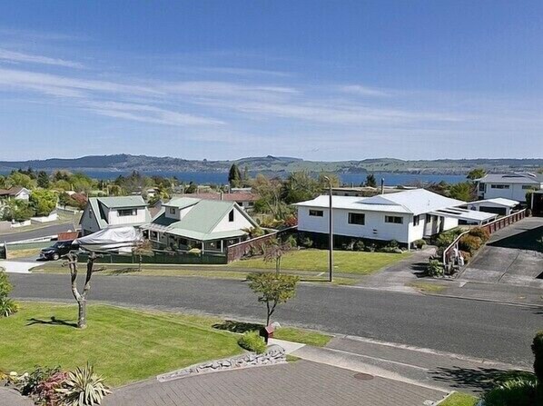 A residential area with houses, a paved road, and a view of hills and water in the distance. - Golders Heights - Taupo Holiday Home (Taupo Central)