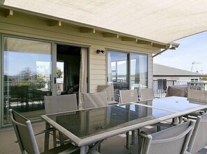 A covered outdoor patio with a glass table and chairs, sliding glass doors, and a view of the surrounding area. - Golders Heights - Taupo Holiday Home (Taupo Central)