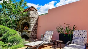 A patio with two lounge chairs, a stone fireplace, and potted plants.