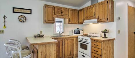 Una cocina con armarios de madera, una estufa blanca, un microondas y un lavamanos.