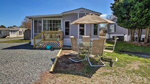 Een gelijkvloers huis met een overdekte patio, een houten trap en een klein terras met stoelen en een tafel.