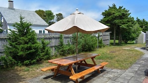 A wooden picnic table with benches and a canopy umbrella in a backyard setting.