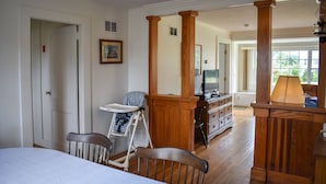 A room with a bed, a wooden chair, a high chair, a television, and a desk with drawers.