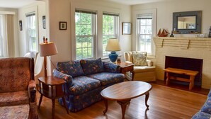 A living room with a blue floral sofa, a wooden coffee table, a patterned armchair, and a fireplace with a brick surround.