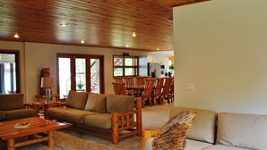 A spacious living room with a wooden ceiling, a sofa, a coffee table, and a dining area with wooden chairs and a table.