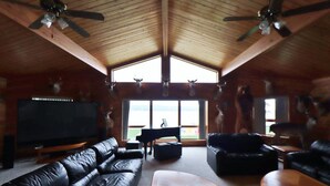 A spacious living room with leather sofas, a wooden coffee table, and a piano.