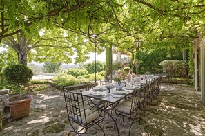 An outdoor dining area with a long table set for a meal, surrounded by trees and greenery. - Fontblanche, Provencal estate for happy reunions (Gordes)