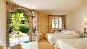A room with two beds, a stone wall, a window with curtains, and a view of greenery outside. - Fontblanche, Provencal estate for happy reunions (Gordes)