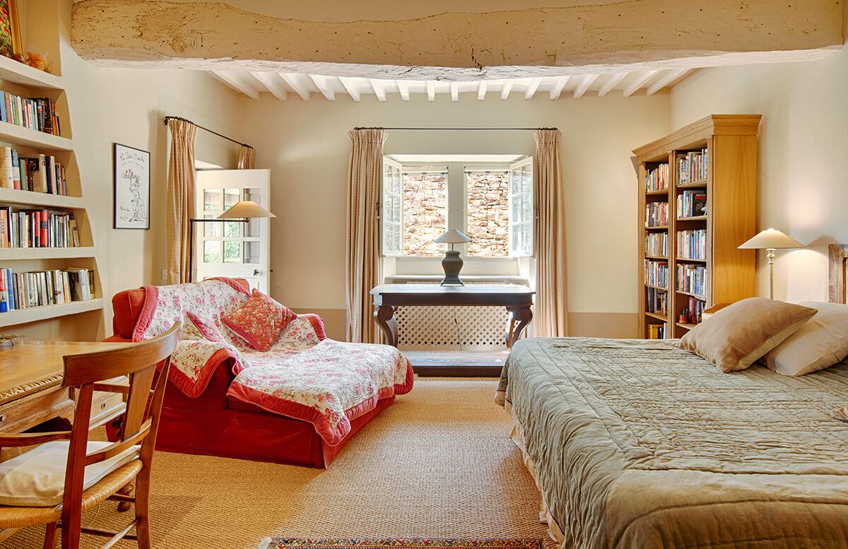 A cozy bedroom with a red sofa, a wooden bed, a desk with a chair, and two bookshelves filled with books.