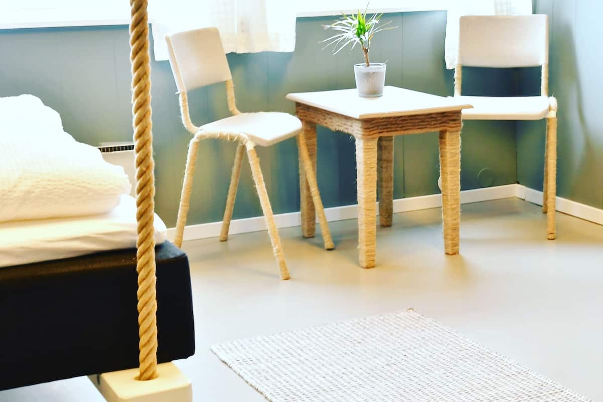 A room with a bed, a hanging chair, a small table with a plant, and a window with curtains.
