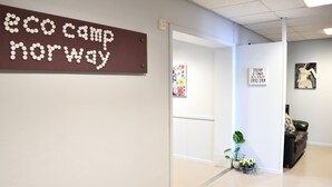 A hallway with a sign reading "eco camp Norway," a potted plant, and artwork on the walls. - Eco Camp Norway - Hostel (Smøla)